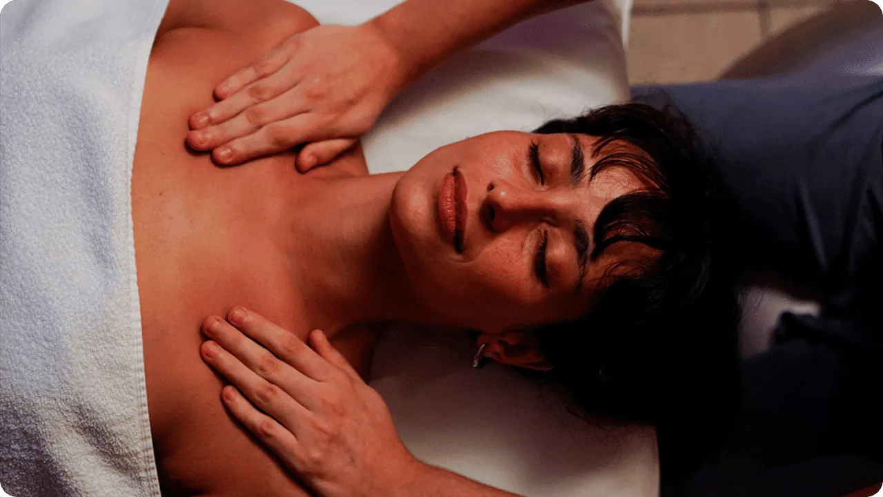 A woman lying on a table in a cozy spa room, receiving a shoulder massage.