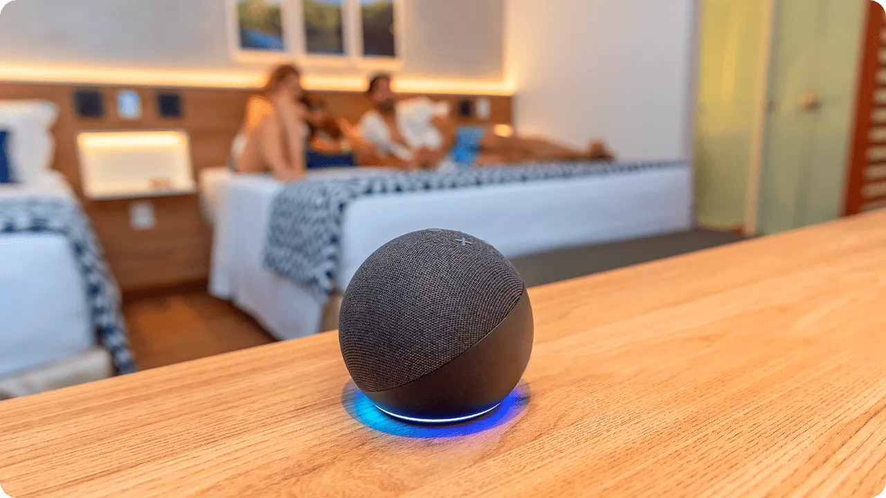 Alexa integrada ao Standard Vitória-Régia, sobre mesa de madeira, em frente às camas onde uma família repousa. 