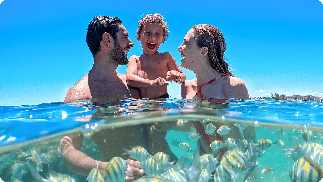 Família com criança aproveitando banho de mar entre peixes coloridos