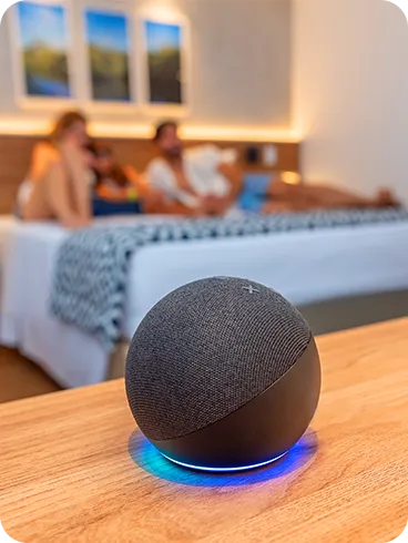 Alexa integrada ao Standard Vitória-Régia, sobre mesa de madeira, em frente às camas onde uma família repousa. 