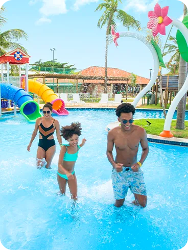 Una familia sonriente corre y juega en la piscina infantil del parque acuático, que cuenta con varios toboganes y coloridas atracciones. Padre, madre e hija disfrutan de un día soleado en el resort.