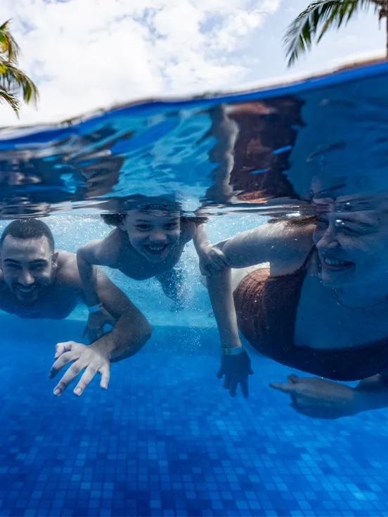 Foto subaquática numa piscina do Salinas Maceió, com família de pai, mãe e filho nadando e sorrindo