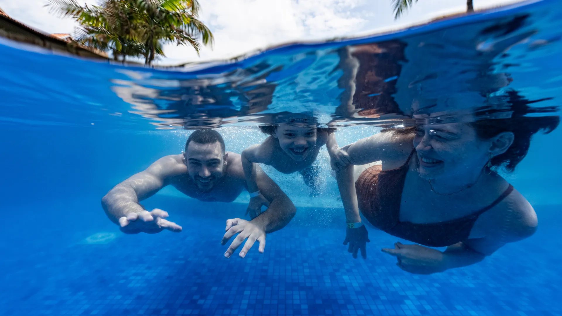 Foto subaquática numa piscina do Salinas Maceió, com família de pai, mãe e filho nadando e sorrindo