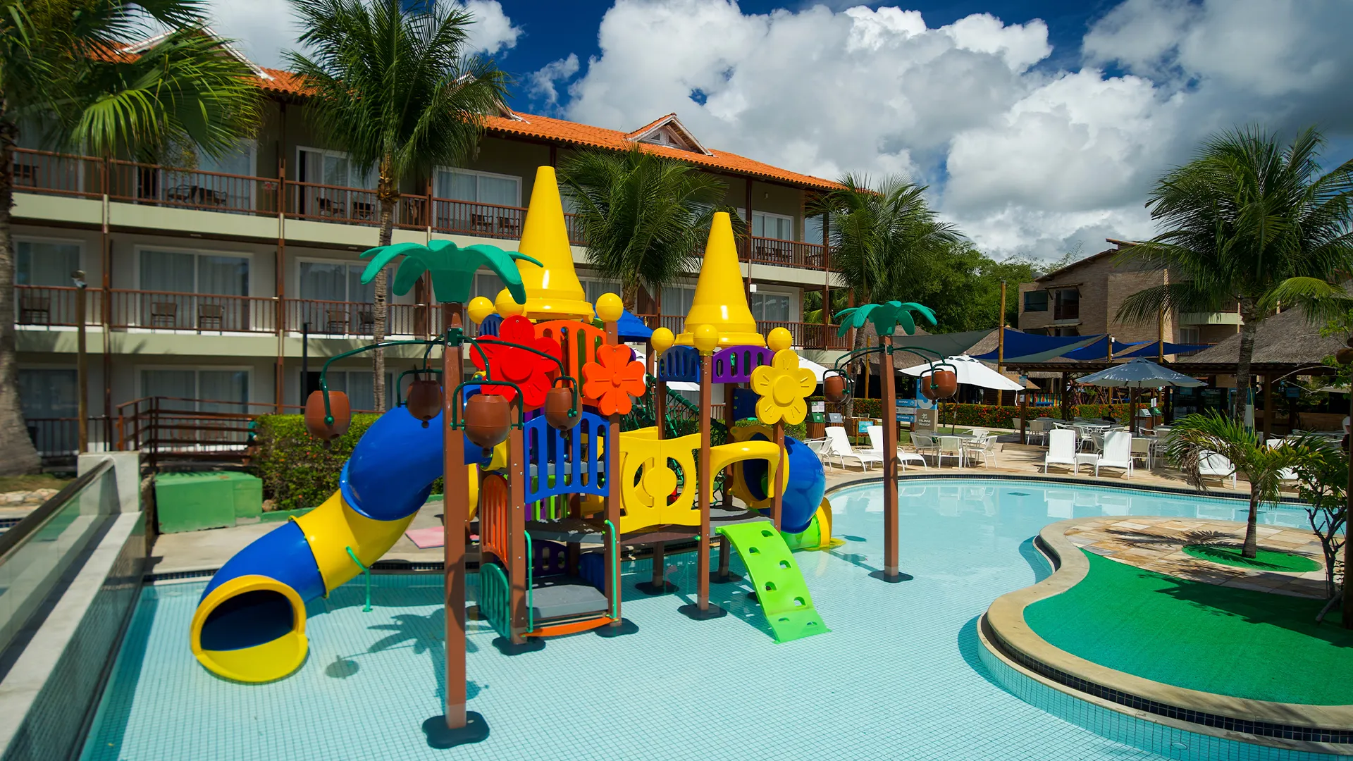 Brinquedão infantil colorido na piscina infantil do Salinas Maceió, ao fundo os apartamentos e área de lazer do resort.