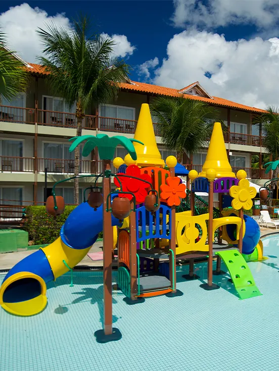 Brinquedão infantil colorido na piscina infantil do Salinas Maceió, ao fundo os apartamentos e área de lazer do resort.