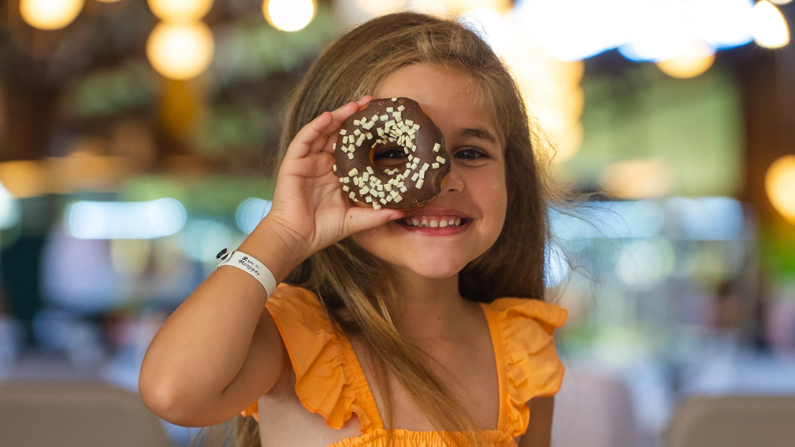 Criança sorridente com vestido laranja mostrando donuts de chocolate do resort Salinas Maragogi.