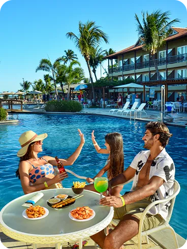 Família se diverte à beira da piscina com bebidas e petiscos variados em mesa de resort All Inclusive