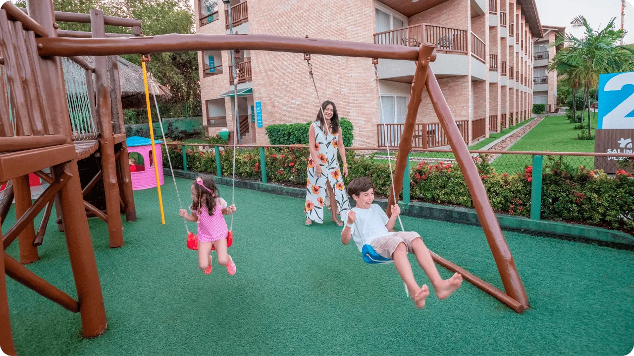 Crianças brincando no parquinho do resort com balanços e brinquedos