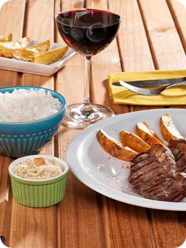Prato de bacalhau e pedaços de carne assada acompanhadas de batatas rústicas, arroz e vinhos.