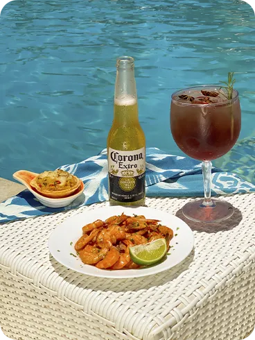Mesa com camarões, limão, petisco assado, cerveja Corona e drink servido à beira da piscina em resort All Inclusive