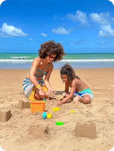 Criança brincando com adulto de fazer castelo de areia na praia