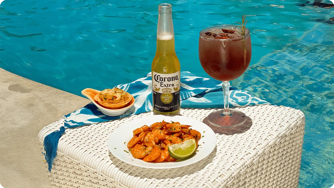 Mesa com camarões, limão, petisco assado, cerveja Corona e drink servido à beira da piscina em resort All Inclusive