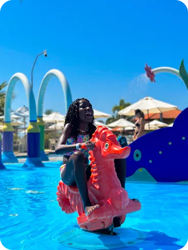 Menina se divertindo em um brinquedo aquático em formato de cavalo-marinho na piscina infantil do resort.