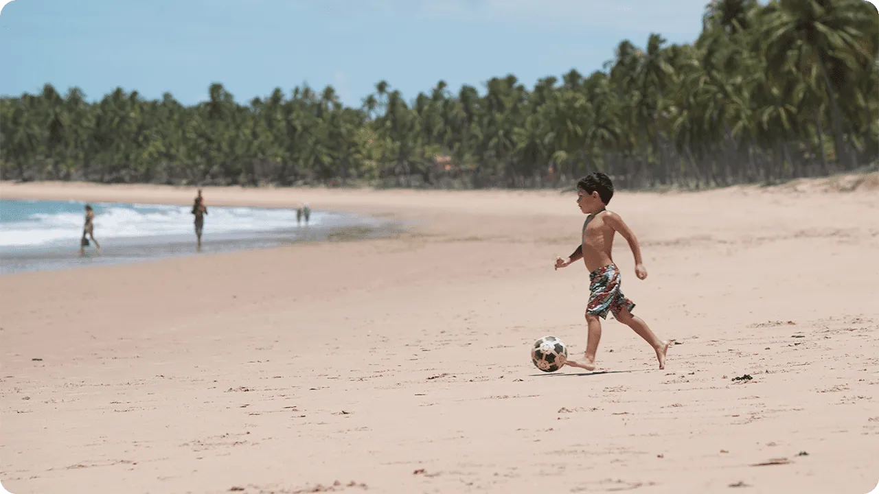 Criança brincando de futebol na areia da praia em dia ensolarado