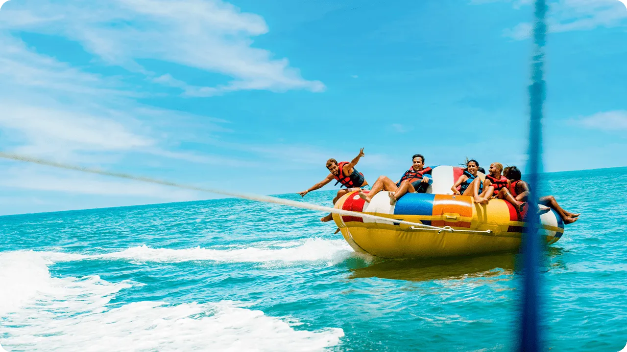 Group of friends on an inflatable tube, known as a Disco Boat, being towed by a speedboat in the Maragogi Sea.