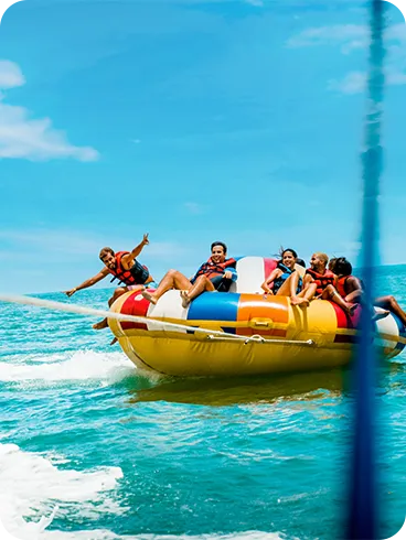Group of friends on an inflatable tube, known as a Disco Boat, being towed by a speedboat in the Maragogi Sea.