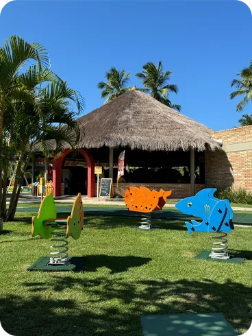 Área externa do resort com balanços e brinquedos coloridos para crianças em meio ao jardim.