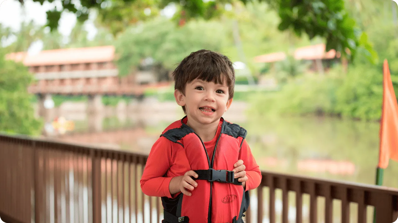 Menino sorridente de colete salva-vidas vermelho, pronto para um passeio no resort.
