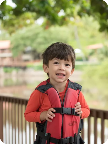 Menino sorridente de colete salva-vidas vermelho, pronto para um passeio no resort.