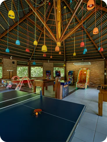 Espaço de jogos com mesas de pingue-pongue, pebolim, fliperamas e brinquedos infantis em resort.