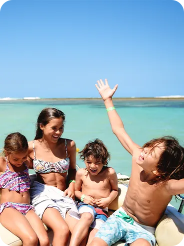 Quatro crianças de diferentes idades sorrindo em um passeio de lancha no mar de águas cristalinas.