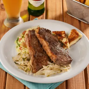 Prato de jantar com carne fatiada sobre massa e risoto, acompanhado de queijo coalho grelhado. A refeição é servida com batata frita e uma cerveja Stella Artois gelada.
