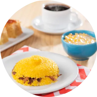 Café da manhã regional com cuscuz recheado, bolo de fubá, munguzá e café preto sobre mesa rústica.