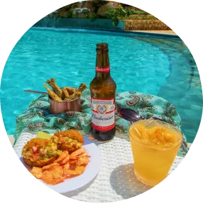 Petiscos variados com camarões empanados, batatas fritas, queijo com linguiça e cerveja gelada sobre bandeja de madeira à beira da piscina.