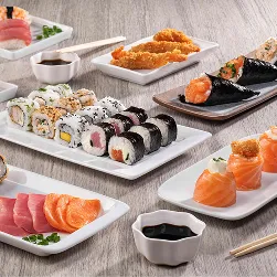 Mesa repleta de sushis: rolinhos variados, niguiris, temakis, sashimis, hot rolls e potes de shoyu com hashis sobre tampo de madeira.