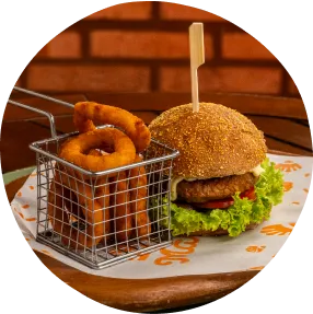 Jantar com hambúrguer artesanal, onion rings crocantes e apresentação rústica sobre mesa de madeira.