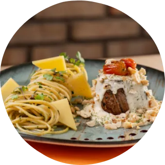 Jantar com espaguete ao molho de ervas, carne ao molho cremoso com tomatinhos assados e vinho tinto sobre uma mesa.