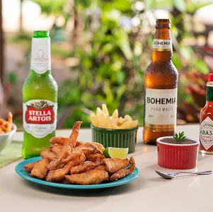 Prato de petiscos fritos com batata, molhos, cervejas e pimenta Tabasco sobre a mesa ao ar livre