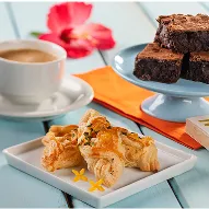 Xícara de café acompanhada de brownies e folhados em prato branco