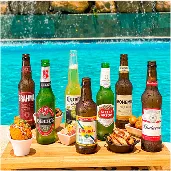 Bandeja à beira da piscina com diversas cervejas geladas, Brahma, Beck’s, Corona, Original, Stella Artois, Bohemia e Budweiser, acompanhadas de petiscos, com cascata de pedras ao fundo.