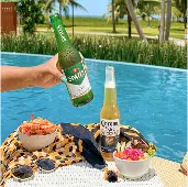 Bandeja à beira da piscina com diversas cervejas geladas, Brahma, Beck’s, Corona, Original, Stella Artois, Bohemia e Budweiser, acompanhadas de petiscos, com cascata de pedras ao fundo.