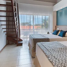 Vista do quarto Apartamento Superior no Salinas Maceió, equipado com duas camas de casal, decoração moderna com parede azul, bancada de trabalho, TV e ar-condicionado.