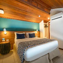 Vista do mezanino do quarto Apartamento Suíte Familiar no Salinas Maceió, equipado com uma cama de casal, parede atrás da cama e teto de madeira, ar-condicionado. No canto direito tem o armário e porta pro banheiro.