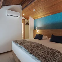 Quarto do resort com cama arrumada e porta da varanda aberta, revelando a vista para o mar azul e os coqueiros do Salinas Maceió.