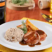 Jantar no Restaurante Galés, na mesa tem garrafa de vinho e uma taça com vinho. Um prato com arroz, uma proteína e batata assada e ao fundo talheres, azeites.