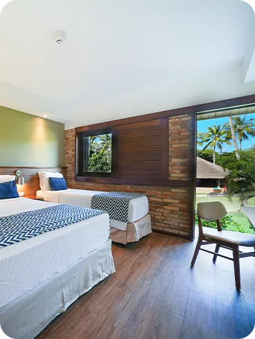 Quarto de hotel Apartamento Standard configurado para três pessoas, com cama de casal e de solteiro, decoração moderna com parede verde e de tijolinhos, e porta da varanda aberta para a área de lazer com coqueiros.