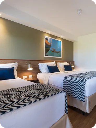 Visão interna do Apartamento Standard triplo, mostrando a cama de casal e a de solteiro, a decoração com parede verde, piso de madeira, ar-condicionado e televisão.