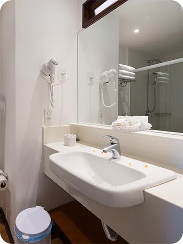 Baño de alojamiento estándar con zona de baño, sanitarios, ducha con control de temperatura, decoración, artículos de aseo O Boticário, toallas, espejo grande y secador de pelo