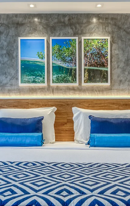 Apartamento Standard Vitória-Régia, uma das acomodações do Salinas Maragogi, com cama uma queen size, banheiro e decoração aconchegante composta por madeira, luminárias e uma composição de quadros de praias de Maragogi.