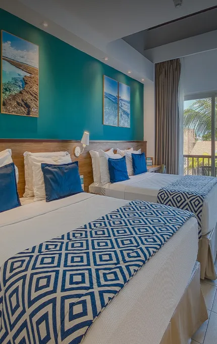 Suíte Familiar, uma das acomodações do Salinas Maceió All Inclusive Resort, com duas camas queen size aconchegantes, painel de madeira atrás delas, com luminária, porta da varanda e escada para o mezanino.