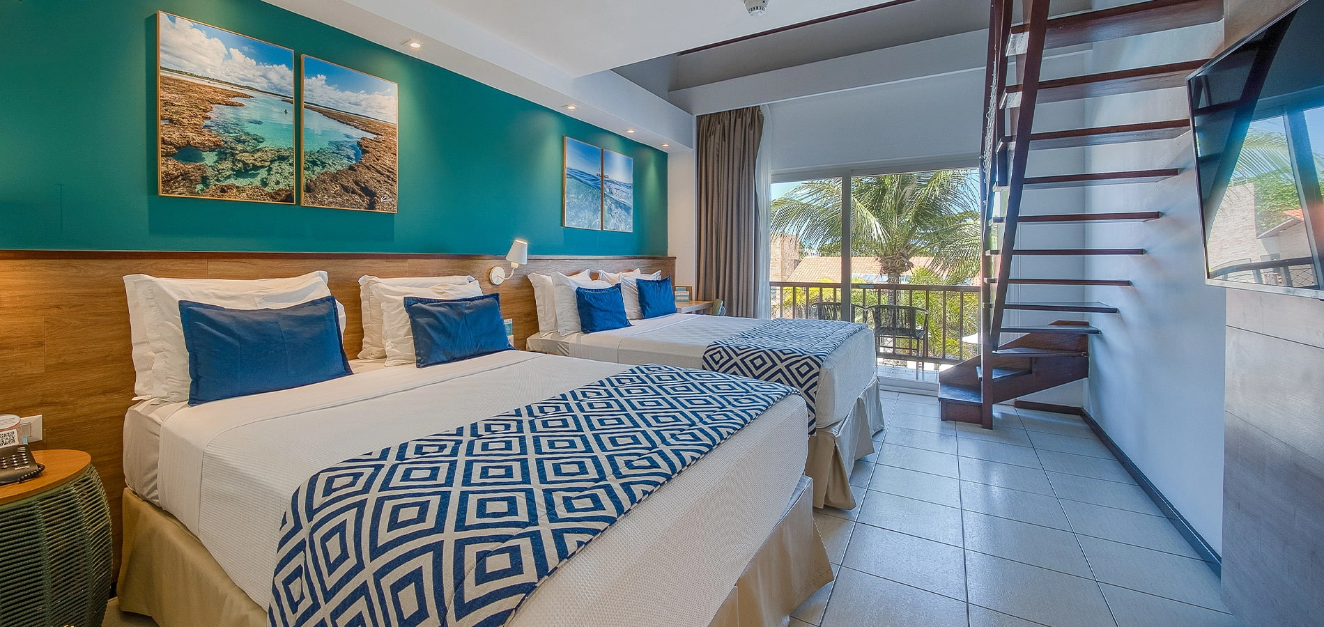 Suíte Familiar, uma das acomodações do Salinas Maceió All Inclusive Resort, com duas camas queen size aconchegantes, painel de madeira atrás delas, com luminária, porta da varanda e escada para o mezanino.