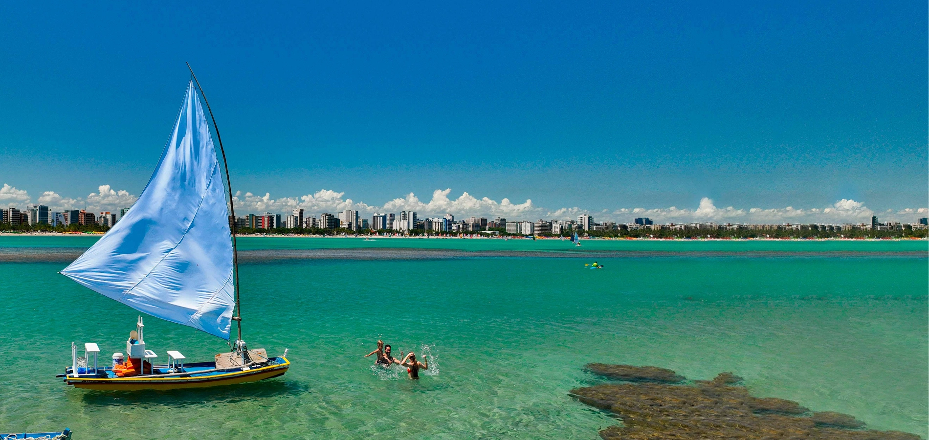Vista das águas cristalinas e jangada em Maceió com a cidade ao fundo
