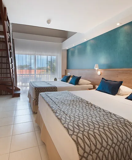 Interior da Suíte Familiar no Salinas Maceió, com duas camas queen size e decoração característica do resort, com dois abajur entre as camas e escada para acesso ao mezanino.
