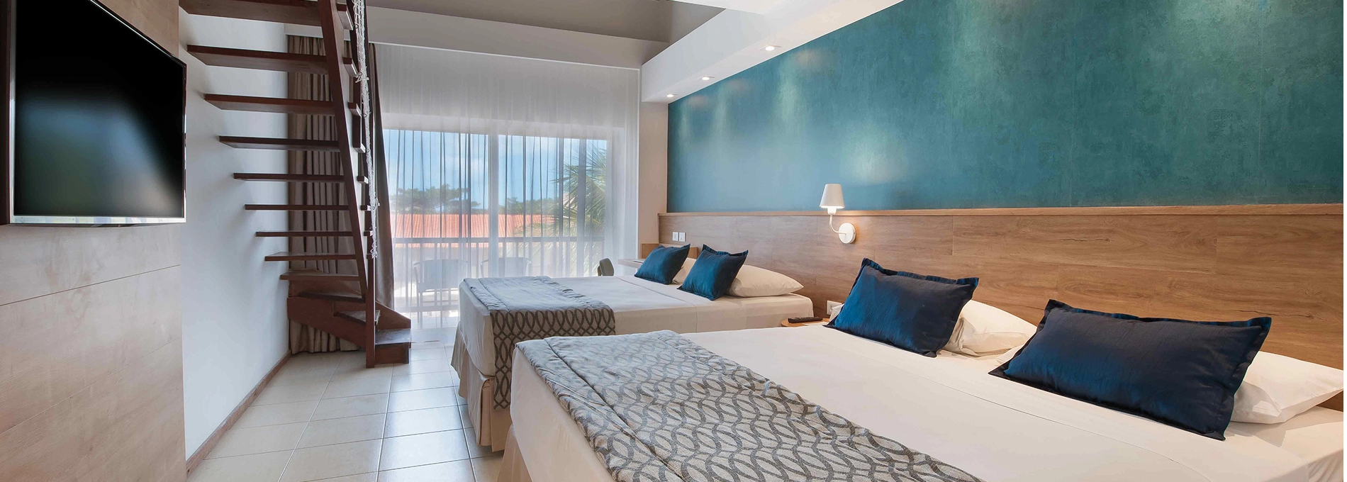 Interior da Suíte Familiar no Salinas Maceió, com duas camas queen size e decoração característica do resort, com dois abajur entre as camas e escada para acesso ao mezanino.