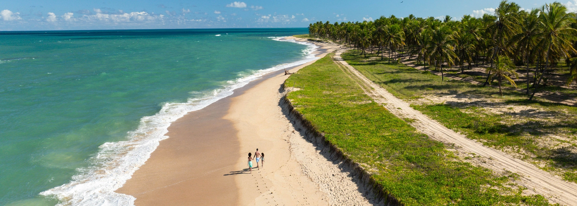 Família caminha sobre areia branca à beira-mar da praia do Gunga, em Alagoas.