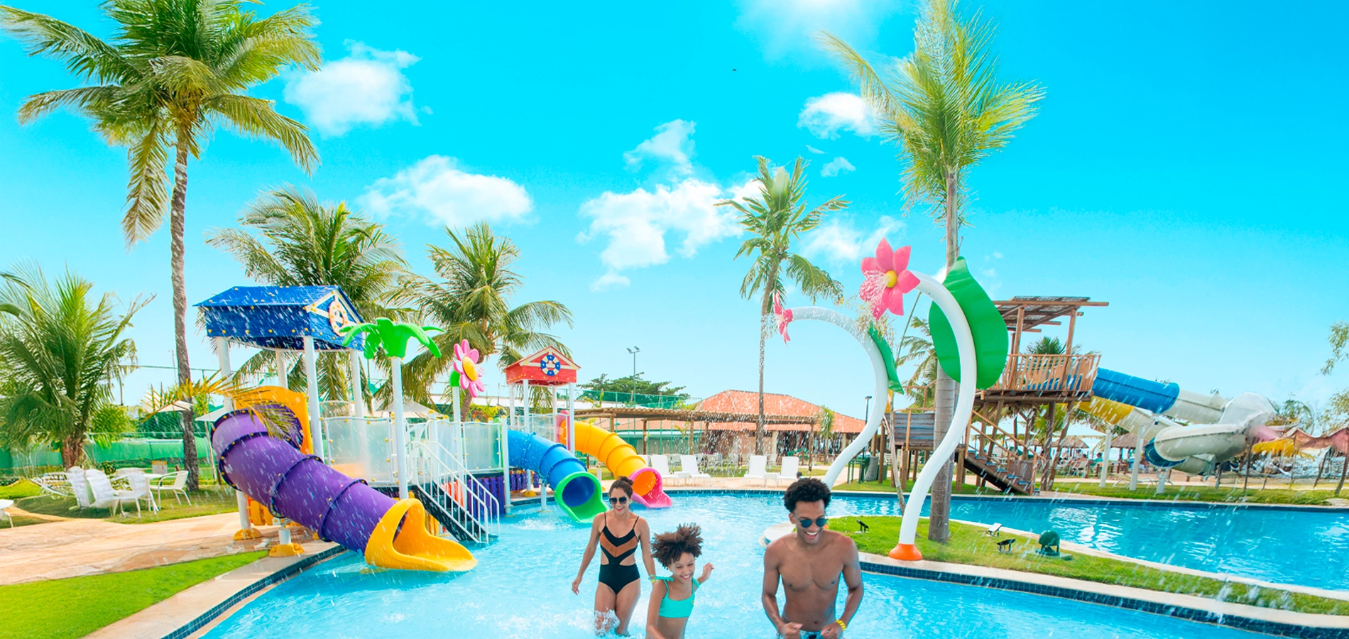 Família se divertindo em piscina infantil com toboáguas coloridos e jatos de água no resort Salinas Maragogi.